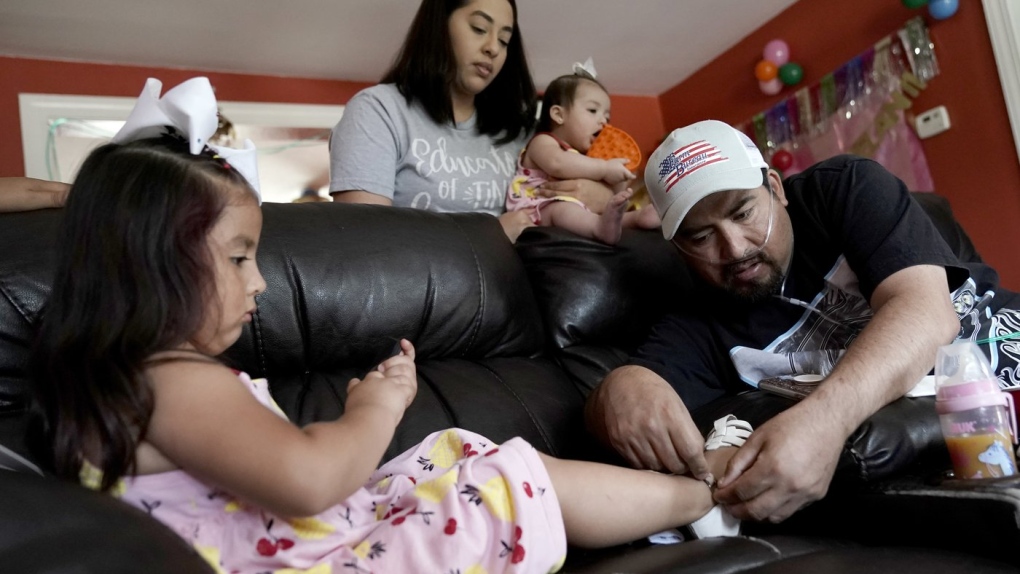 Freddy Fernandez buckles the shoes of his 4-year-old daughter, Melanii, while his fiancé, Vanessa Cruz, holds their 8-month-old daughter Mariana Friday, June 10, 2022, at their home in Carthage, Mo. (AP Photo/Charlie Riedel)