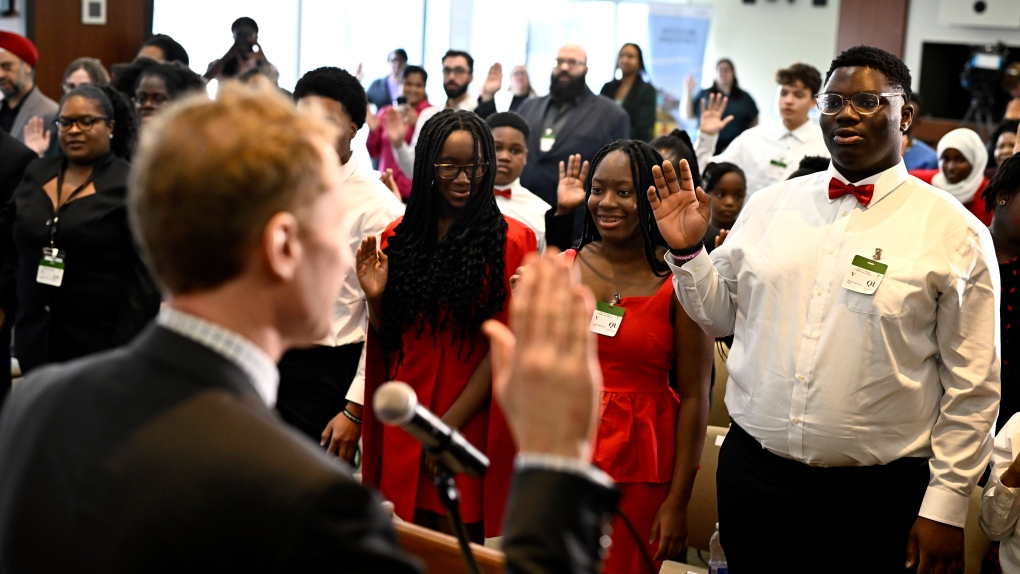 New Canadians raise their right hands as Minister of Immigration, Refugees and Citizenship Marc Miller, left, administers the Oath of Citizenship, during a citizenship ceremony in Ottawa, on Wednesday, Feb. 28, 2024. (Justin Tang/THE CANADIAN PRESS)