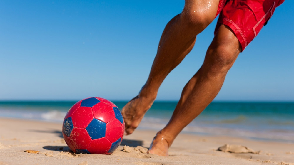 Man kicking soccer ball on beach