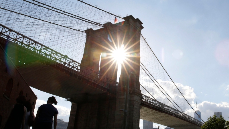 People walk beneath the 113 year-old Brooklyn Bridge as the sun peeks through one of the bridge's granite towers, Thursday, June 30, 2016, at Brooklyn Bridge Park in New York. (AP Photo/Kathy Willens)