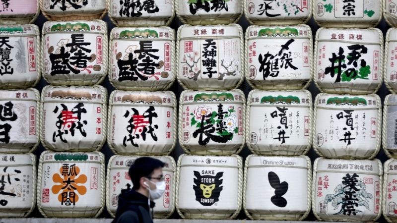 A man in a facemask walks past barrels of sake at the entrance to Meiji shrine in Tokyo. (AFP)