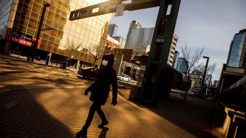 A pedestrian wearing a mask walks down the empty streets of downtown Edmonton as people stay in to protect against getting the COVID-19 virus, in Edmonton on Sunday March 22, 2020. THE CANADIAN PRESS/Jason Franson