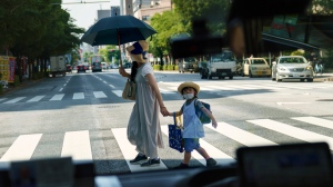 A pedestrian crossing a street with a child is seen through a taxi window in Tokyo, Monday, July 19, 2021. (David Goldman / AP Photo, File)