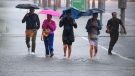 People hold umbrellas as they make their way through water pooling in an intersection as heavy rain pours down in Ottawa, on Thursday, June 6, 2024. (Justin Tang/THE CANADIAN PRESS)