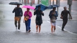 People hold umbrellas as they make their way through water pooling in an intersection as heavy rain pours down in Ottawa, on Thursday, June 6, 2024. (Justin Tang/THE CANADIAN PRESS) 
