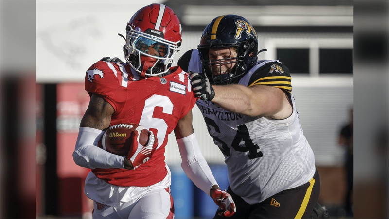 Hamilton Tiger-Cats offensive lineman Coulter Woodmansey (64) reaches for Calgary Stampeders defensive back Demerio Houston (6) after an interception during first half CFL football action in Calgary, Friday, June 7, 2024. THE CANADIAN PRESS/Jeff McIntosh