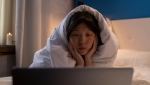 FILE: A woman watches a movie on her computer while wrapped in a blanket. (Ron Lach / Pexels)