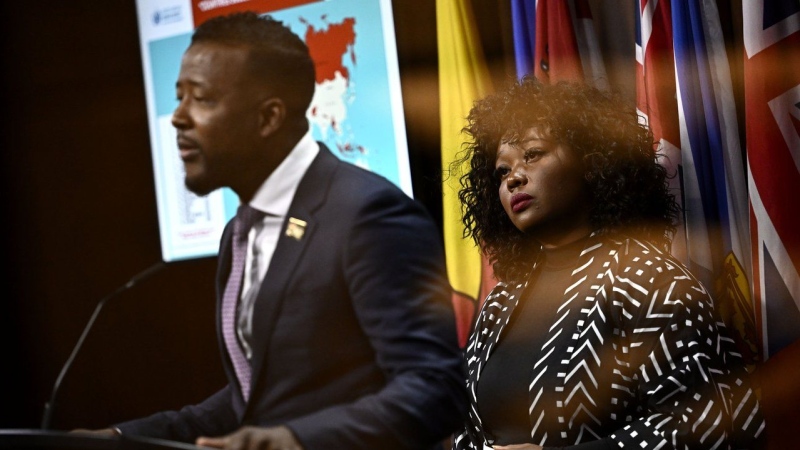 Bernadeth Betchi, CHRC employee and representative plaintiff, listens as Nicholas Marcus Thompson, executive director of the Black Class Action Secretariat, speaks at a news conference. (Justin Ting/The Canadian Press)