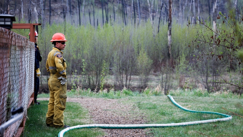 A firefighter monitors a wildfire sprinkler hose in the evacuated neighbourhood of Grayling Terrace in Fort McMurray, Alta., Thursday, May 16, 2024. (Jeff McIntosh / The Canadian Press)