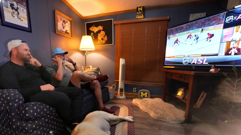 Bob Madden, center, and his son Jonathan, left, watch the Stanley Cup hockey final from a couch, Monday, June 10, 2024 in Genoa Township, Mich. Madden is deaf and he was enjoying the view with access to the commentary delivered in American Sign Language for the first time during a sporting event. The NHL became the first major sports league to offer play by play and analysis in ASL during a live broadcast. (Carlos Osorio / The Associated Press)