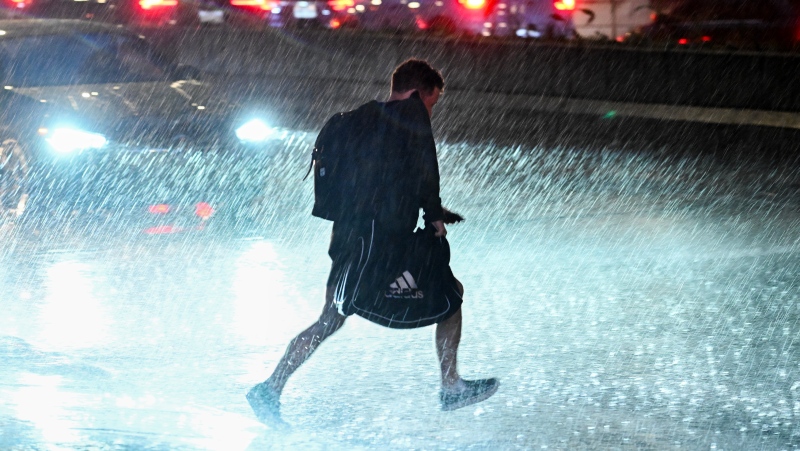 A person makes their way across a street during heavy rainfall in Montreal, Thursday, June 6, 2024, as a severe thunderstorm warning was issued for the region. (Graham Hughes / The Canadian Press)