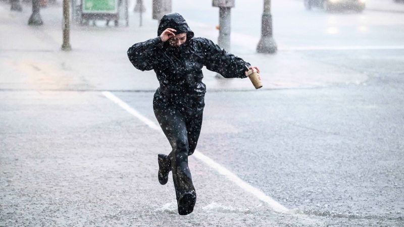A person leaps past water flooding an intersection as heavy rain pours down in Ottawa, on Thursday, June 6, 2024. (Justin Tang / The Canadian Press)