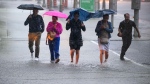 People hold umbrellas as they make their way through water pooling in an intersection as heavy rain pours down in Ottawa, on Thursday, June 6, 2024. (Justin Tang / The Canadian Press)