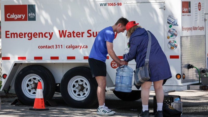 Ian Dyer fills a water jug with help from a friend at an emergency supply provided by the city as work to repair a major water main stretches into a second day in Calgary, Friday, June 7, 2024.THE CANADIAN PRESS/Jeff McIntosh