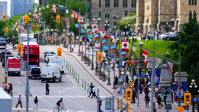 People make their way along Wellington Street below Canada and Provincial Flags hung for Canada Day in Ottawa on Thursday, June 27, 2024. (Sean Kilpatrick/THE CANADIAN PRESS)