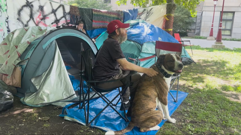 Paul, a man experiencing homelessness, sits outside a tent with a dog on the campus of the University of Ottawa on July, 8 2024. (Jackie Perez/CTV News Ottawa)