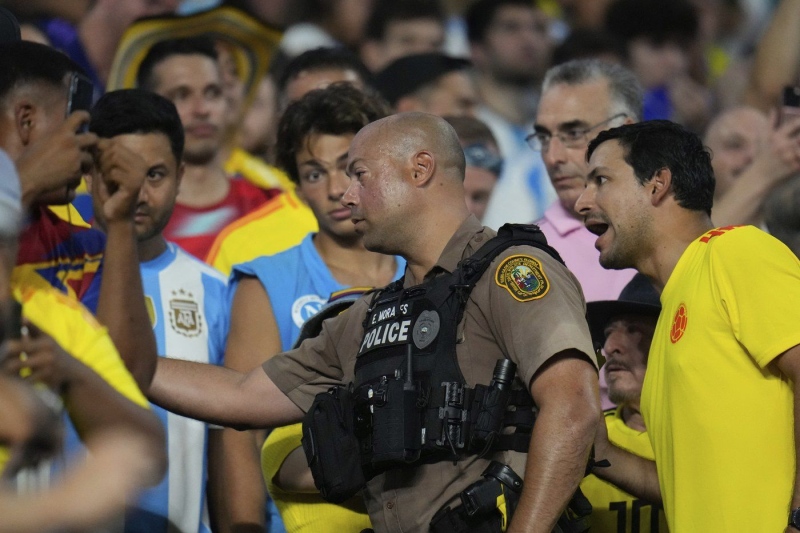 A police officer talks to fans in the stands during the Copa America final soccer match between Argentina and Colombia in Miami Gardens, Fla., Sunday, July 14, 2024. (AP Photo/Julio Cortez)