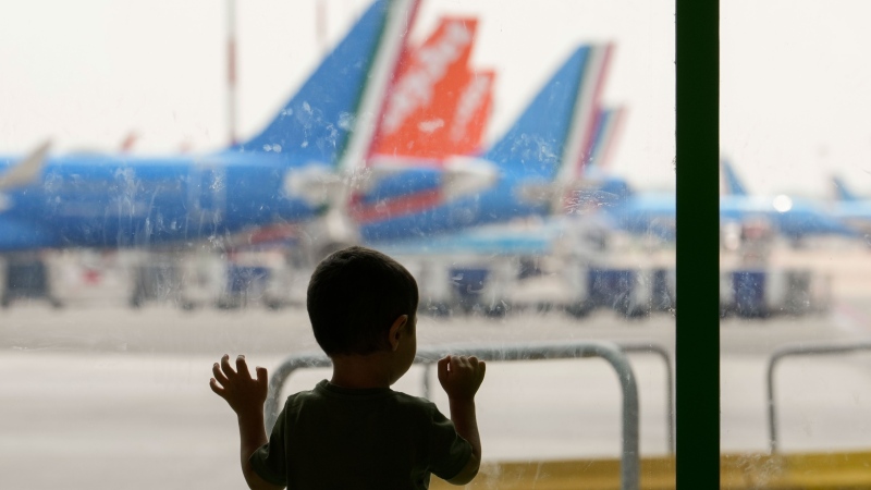 A kid watches aircrafts from a window as he waits at a gate of the Linate airport in Milan, Italy, Friday, July 19, 2024 as many flights have been delayed or cancelled due to the worldwide internet outage.