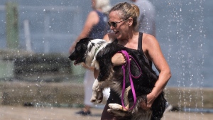 A woman carries her dog through a water fountain on the Halifax Waterfront in Halifax on Thursday, July 6, 2023. THE CANADIAN PRESS/Darren Calabrese