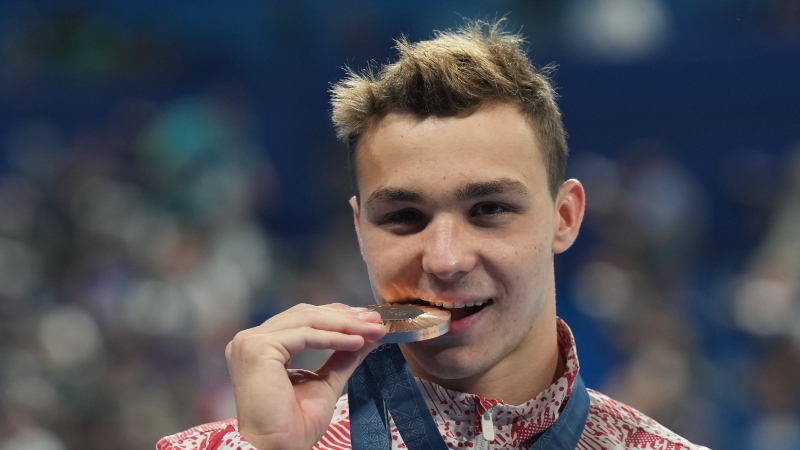 Ilya Kharun, of Canada, bites down on his bronze medal after competing in the men's 200-metre butterfly final at the 2024 Summer Olympics in Nanterre, France on Wednesday, July 31, 2024. THE CANADIAN PRESS/Nathan Denette