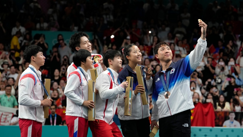 South Korea's Lim Jonghoon, right, takes a selfie with North Korea's Ri Jong Sik, left, and Kim Kum, second left, China's Wang Chuqin, background, and Sun Yingsha, centre, and his teammate Shin Yubin, right, and Lim Jonghoon during the medal ceremony at the 2024 Summer Olympics, July 30, 2024, in Paris, France. (AP Photo/Petros Giannakouris, File)