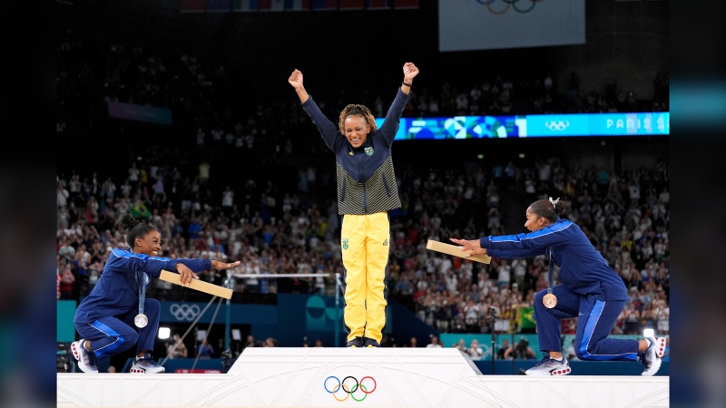 American gymnasts Simone Biles, left, and Jordan Chiles bow to Brazil's gold medallist Rebeca Andrade during the medal ceremony in Paris on Aug. 5, 2024. (Abbie Parr / AP Photo)