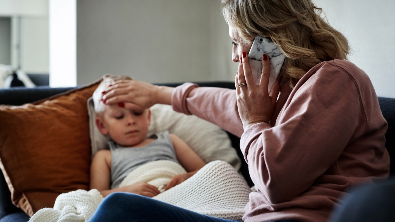 A mother making a phone call while aiding to her sick young son at home. (Getty)