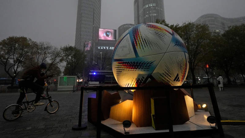 A man and a child on a bicycle look at the giant replica football placed to promote the Qatar FIFA World Cup in Beijing, Nov. 20, 2022. (AP Photo/Ng Han Guan)