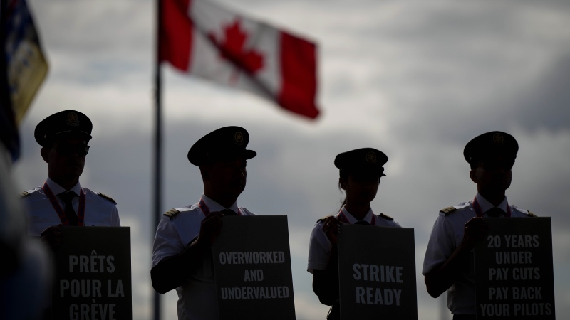 Air Canada pilots air silhouetted while holding signs during an informational picket at Vancouver International Airport in Richmond, B.C., on Tuesday, August 27, 2024. (Darryl Dyck / The Canadian Press)