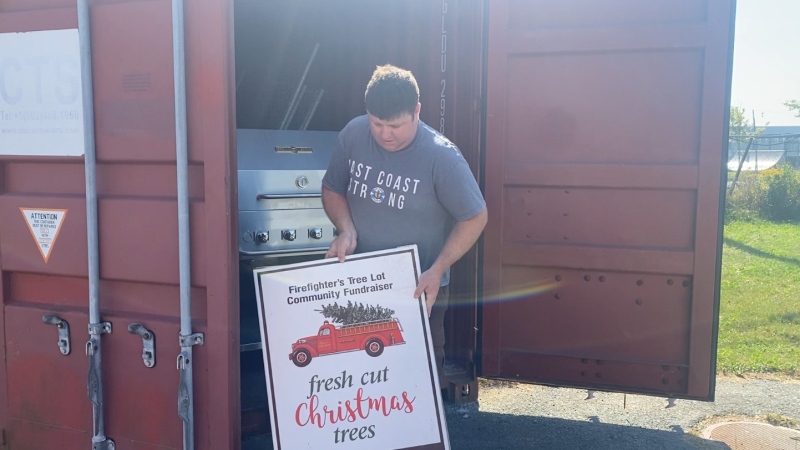 A member of the Eastern Passage Cow Bay Firefighters Association removes a sign from a shipping container that advertises a firefighter's Christmas tree community fundraiser.