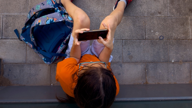 A 11-year-old boy plays with his father's phone outside school in Barcelona, Spain, Monday, June 17, 2024. (Emilio Morenatti / The Associated Press)