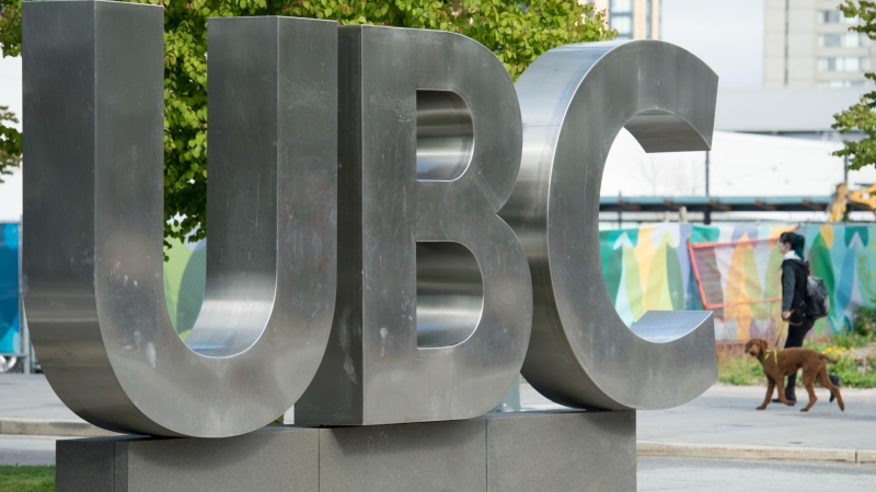 A woman and her dog walk past the UBC sign at the University of British Columbia in Vancouver, April 23, 2019. (Jonathan Hayward / The Canadian Press)