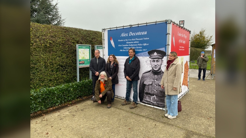 Part of a group stands in front of a photo of Alex Decoteau, at Tyne Cot Cemetery in Belgium. (Derek Haggett/CTV Atlantic)