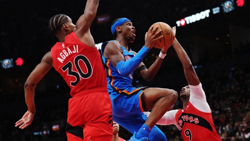 Oklahoma City Thunder's Shai Gilgeous-Alexander (centre) drives between Toronto Raptors' Ochai Agbaji (30) and RJ Barrett (9) during second-half NBA action in Toronto on Thursday, December 5, 2024. THE CANADIAN PRESS/Nathan Denette