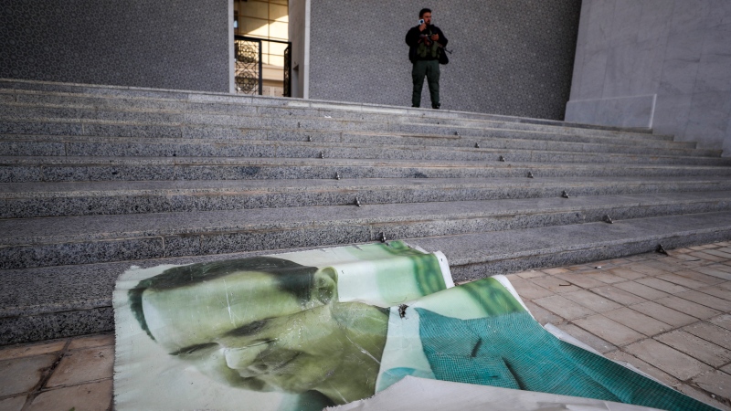 A giant picture of Syrian President Bashar Assad lies on the ground as a Syrian opposition fighter stands nearby, inside the Presidential Palace in Damascus, Syria, Sunday, Dec. 8, 2024. (AP Photo/Omar Sanadiki)