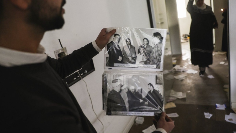 A man shows old pictures of the late Syrian President Hafez Assad as civilians ransack the private residence on Sunday, Dec. 8, 2024. (AP Photo/Ghaith Alsayed,File)