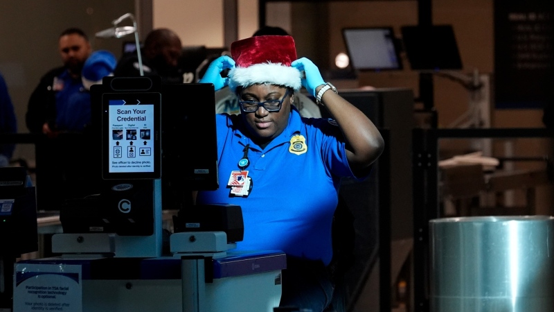 A TSA agent adjusts their holiday hat between checking traveller's documents through in line for security at Love Field airport in Dallas, Friday, Dec. 20, 2024. (AP Photo/LM Otero)