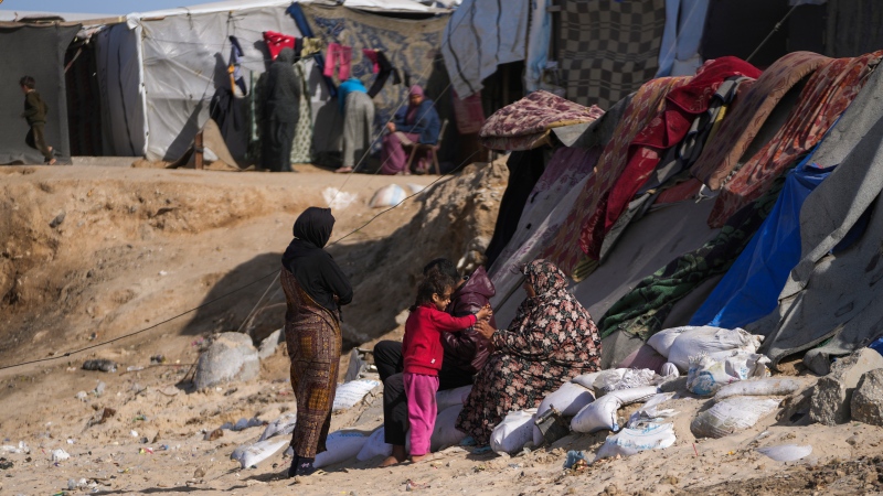 Palestinian families sit outside of tents made locally from pieces of cloth and nylon, in a camp for internally displaced Palestinians at the beachfront in Deir al-Balah, central Gaza Strip, Friday, Dec. 27, 2024. (AP Photo/Abdel Kareem Hana)