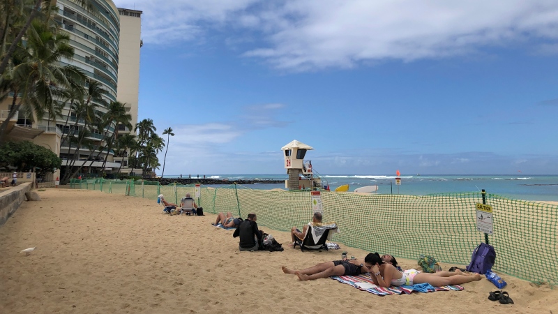 In this file photo, People sit behind a fenced off area of Kaimana Beach in Honolulu, Thursday, April 20, 2023.