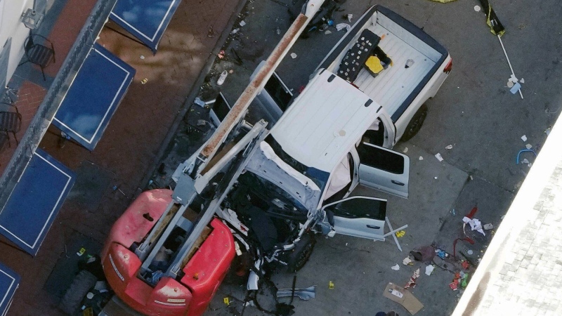 A black flag with white lettering lies on the ground rolled up behind a pickup truck that a man drove into a crowd on Bourbon Street in New Orleans, killing and injuring a number of people, early Wednesday morning, Jan. 1, 2025. (AP Photo/Gerald Herbert)