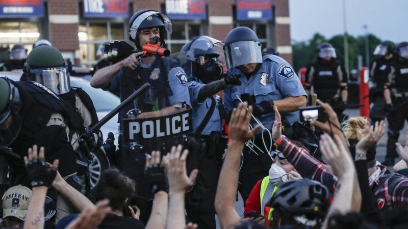 A police officer points a hand cannon at protesters who have been detained pending arrest on South Washington Street in Minneapolis, May 31, 2020, as protests continued following the death of George Floyd. (AP Photo/John Minchillo, File)