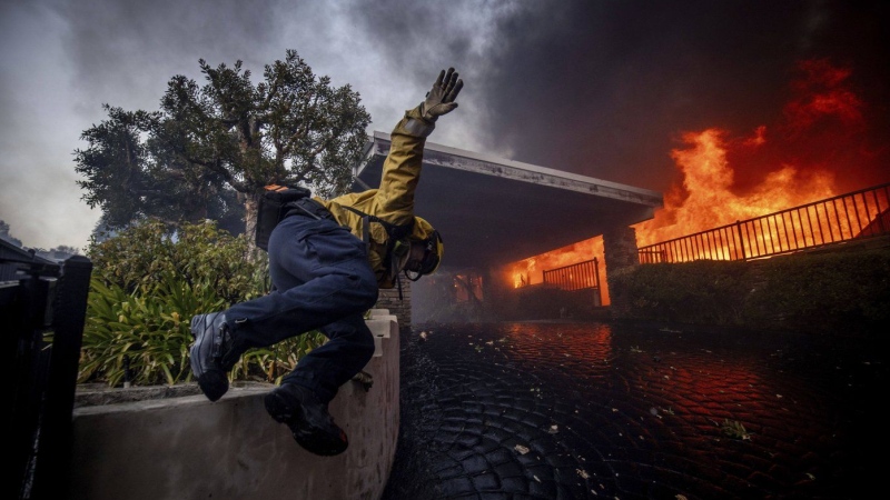 A firefighter jumps over a fence while fighting the Palisades Fire in the Pacific Palisades neighborhood of Los Angeles, Tuesday, Jan. 7, 2025. (Ethan Swope / The Associated Press)