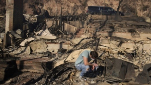 Luke Dexter kneels as he sifts through the remains of his father's fire-ravaged beach front property in the aftermath of the Palisades Fire on Friday, Jan. 10, 2025, in Malibu, Calif. (AP Photo/John Locher)