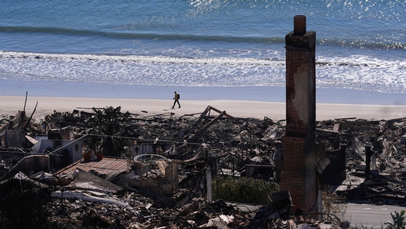 A person walks along a beach past homes destroyed by the Palisades Fire along the Pacific Coast Highway in Malibu, Calif., Jan. 12, 2025. (AP Photo/Mark J. Terrill)