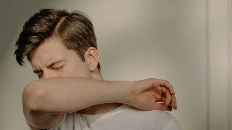 A man coughing into his arm. (Pexels) 