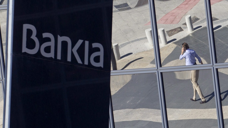 A man is seen reflected in the glass building of the Bankia bank headquarters in Madrid, Wednesday May 9, 2012. (AP Photo/Paul White)